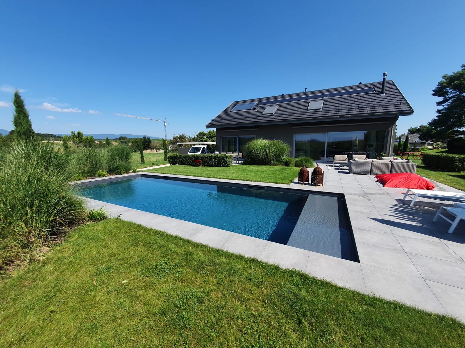 Piscine béton PVC anthracite au reflet bleu profond devant une maison contemporaine grise