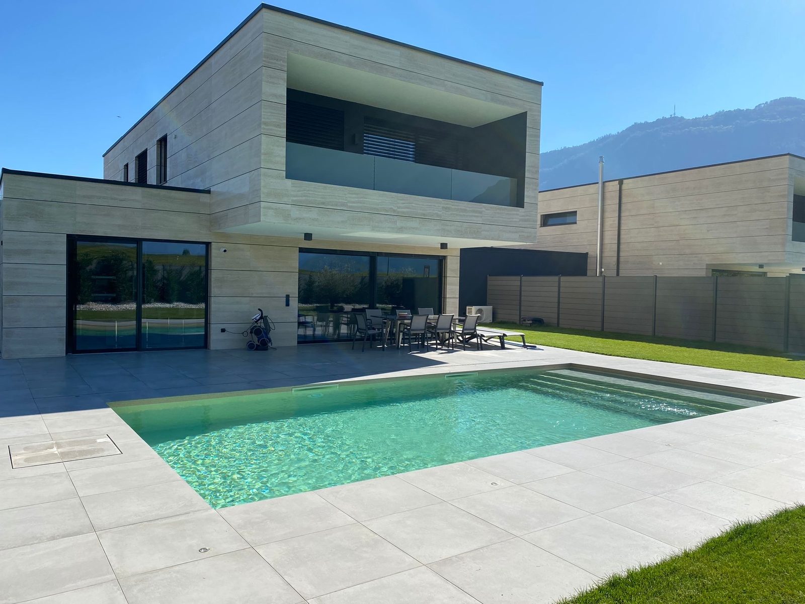 Villa contemporaine en travertin avec piscine béton au liner sable, eau vert lagon et montagnes valaisannes