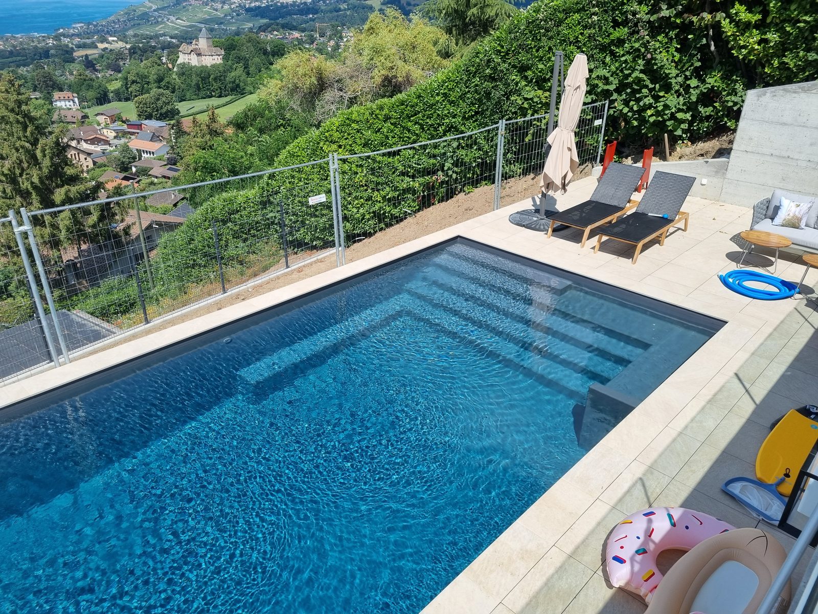 Piscine béton à membrane armée anthracite surplombant le lac Léman, escalier immergé et terrasse en travertin