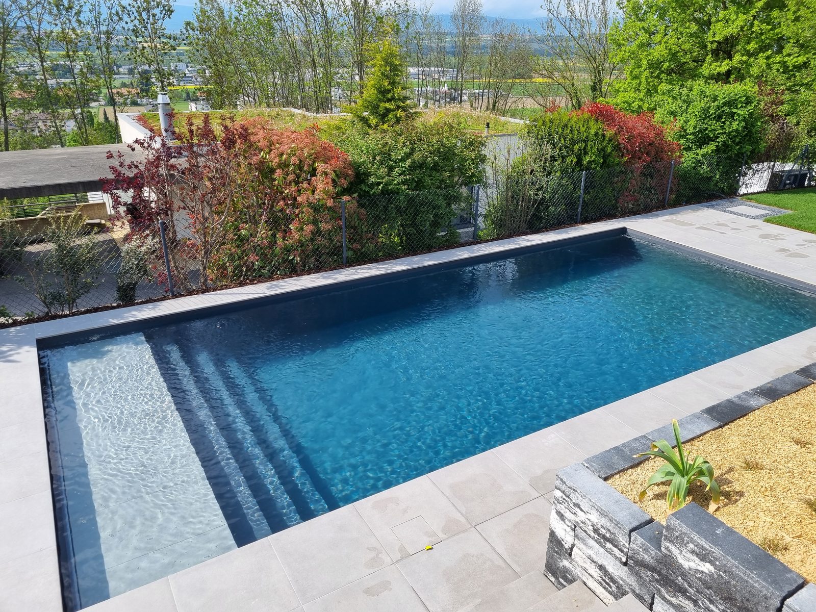 Piscine béton au liner gris anthracite avec banquette immergée et escalier, eau scintillante au soleil