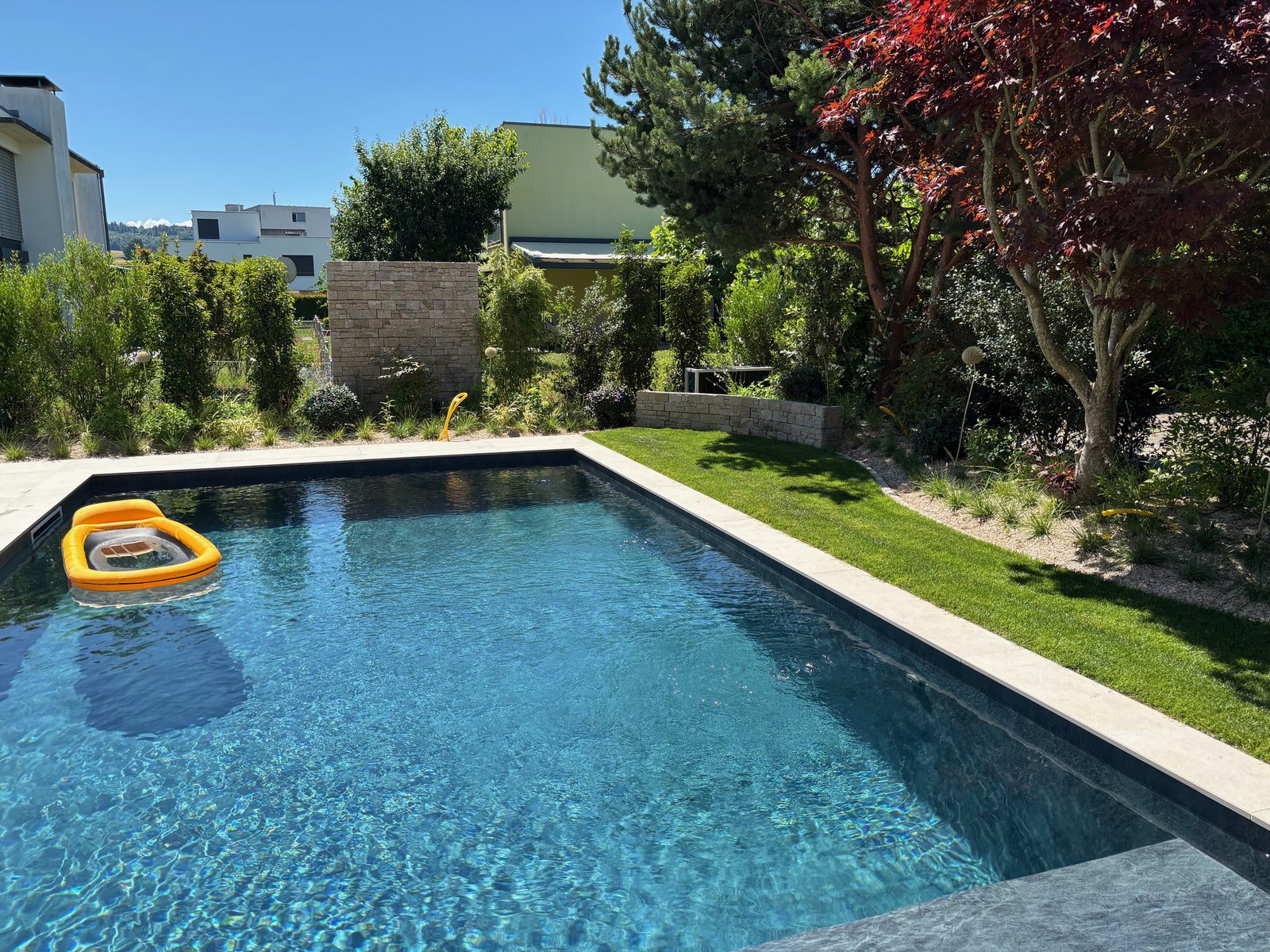 Piscine béton à liner PVC 3D gris anthracite, eau bleu profond, érable rouge et mur en pierre