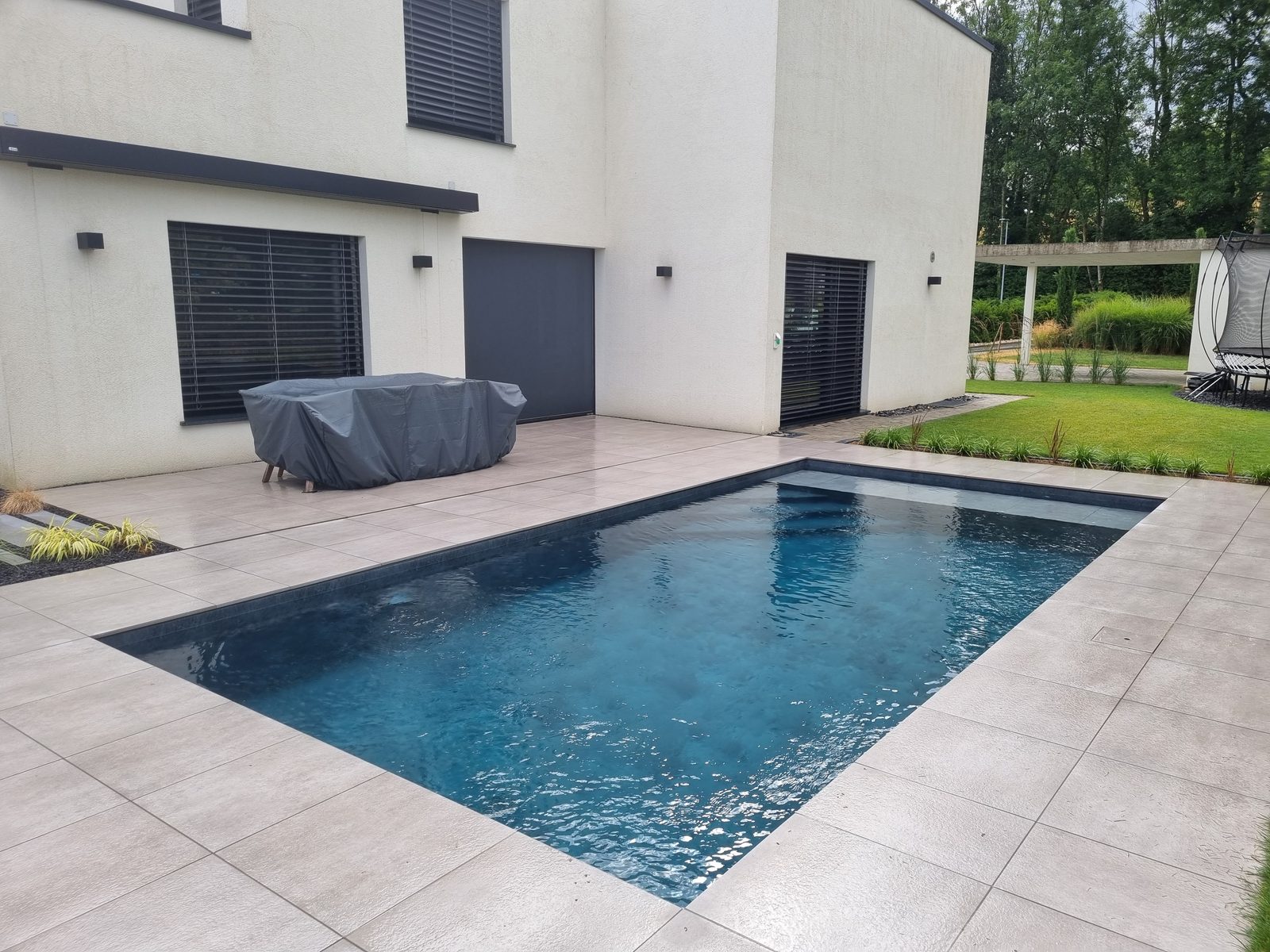 Piscine anthracite au pied d'une villa moderne blanche, grande terrasse en grès cérame