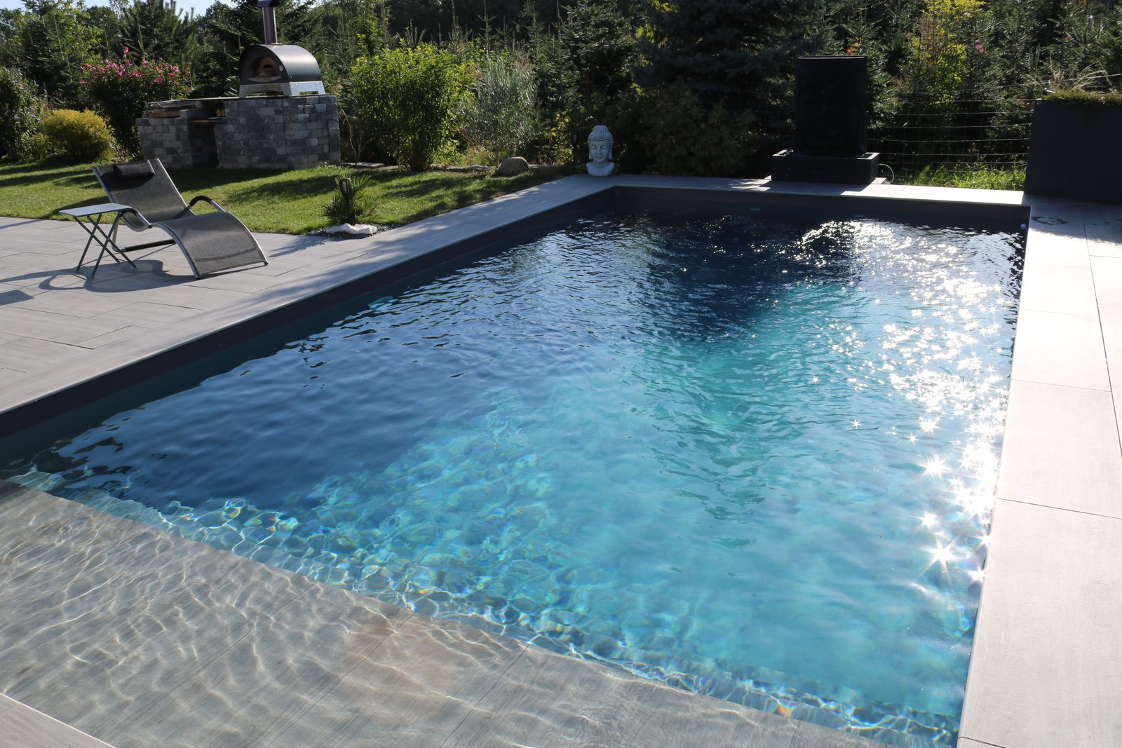 Piscine béton à liner gris anthracite scintillant au soleil, plage immergée au premier plan