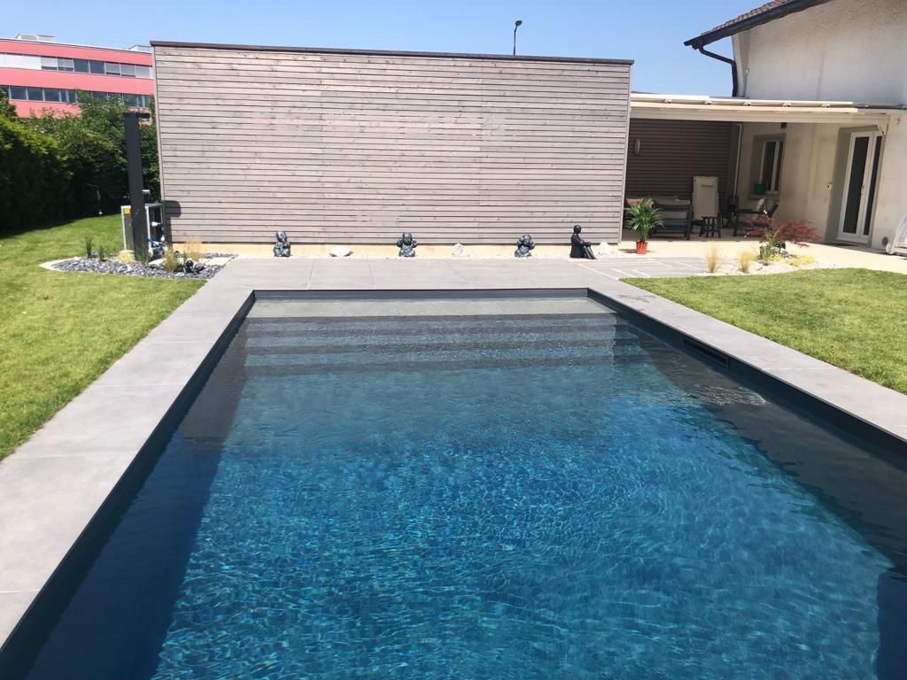 Piscine béton PVC anthracite, eau bleu profond scintillante, mur en bois et terrasse grise