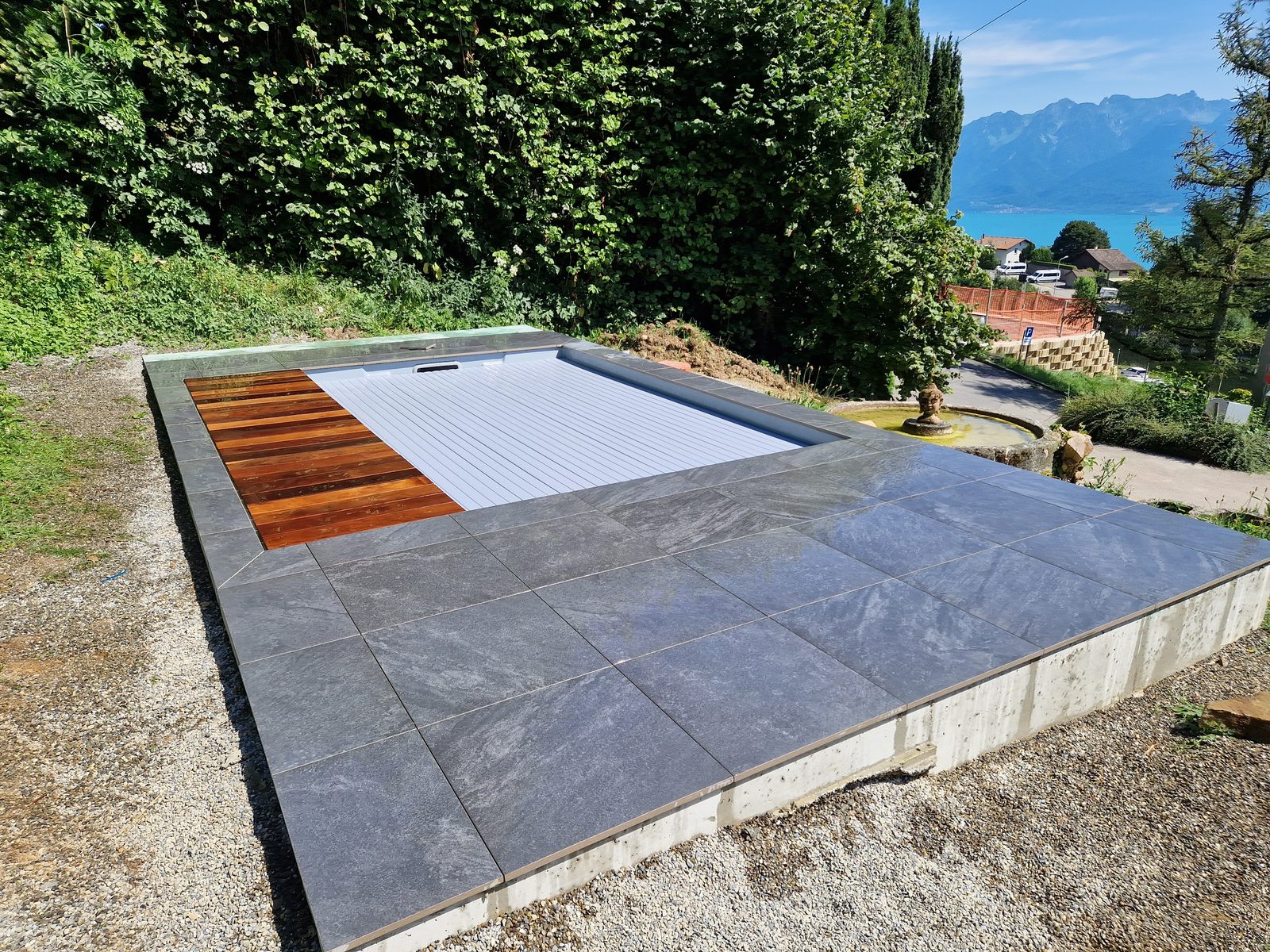 Piscine coque avec volet roulant et terrasse en grès cérame, vue plongeante sur le lac Léman et les Alpes