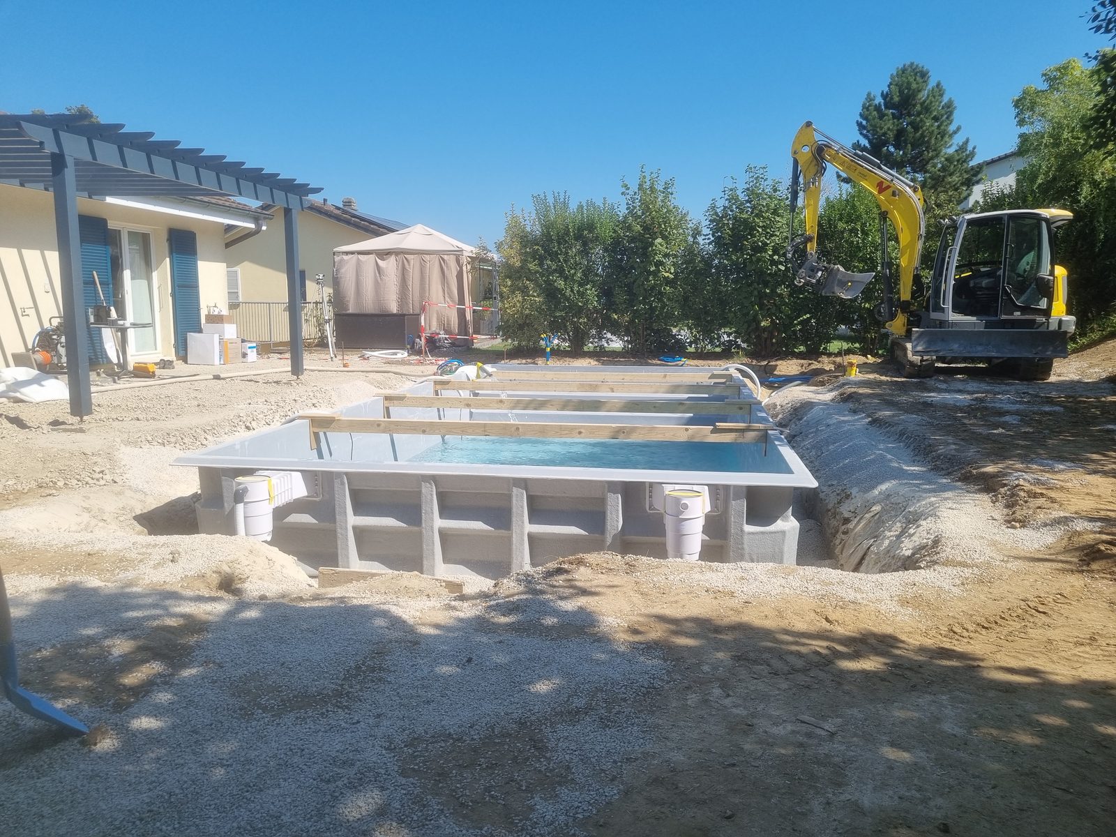Fibreglass pool installation by Swiss Piscine: shell set in the excavation, backfilling in progress