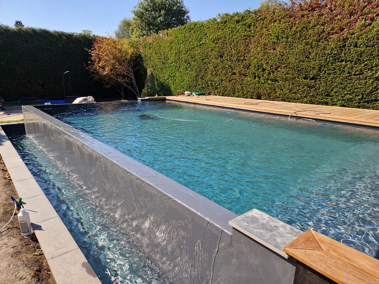Piscine à débordement anthracite, eau turquoise limpide, lame d'eau s'écoulant sur le mur de débordement