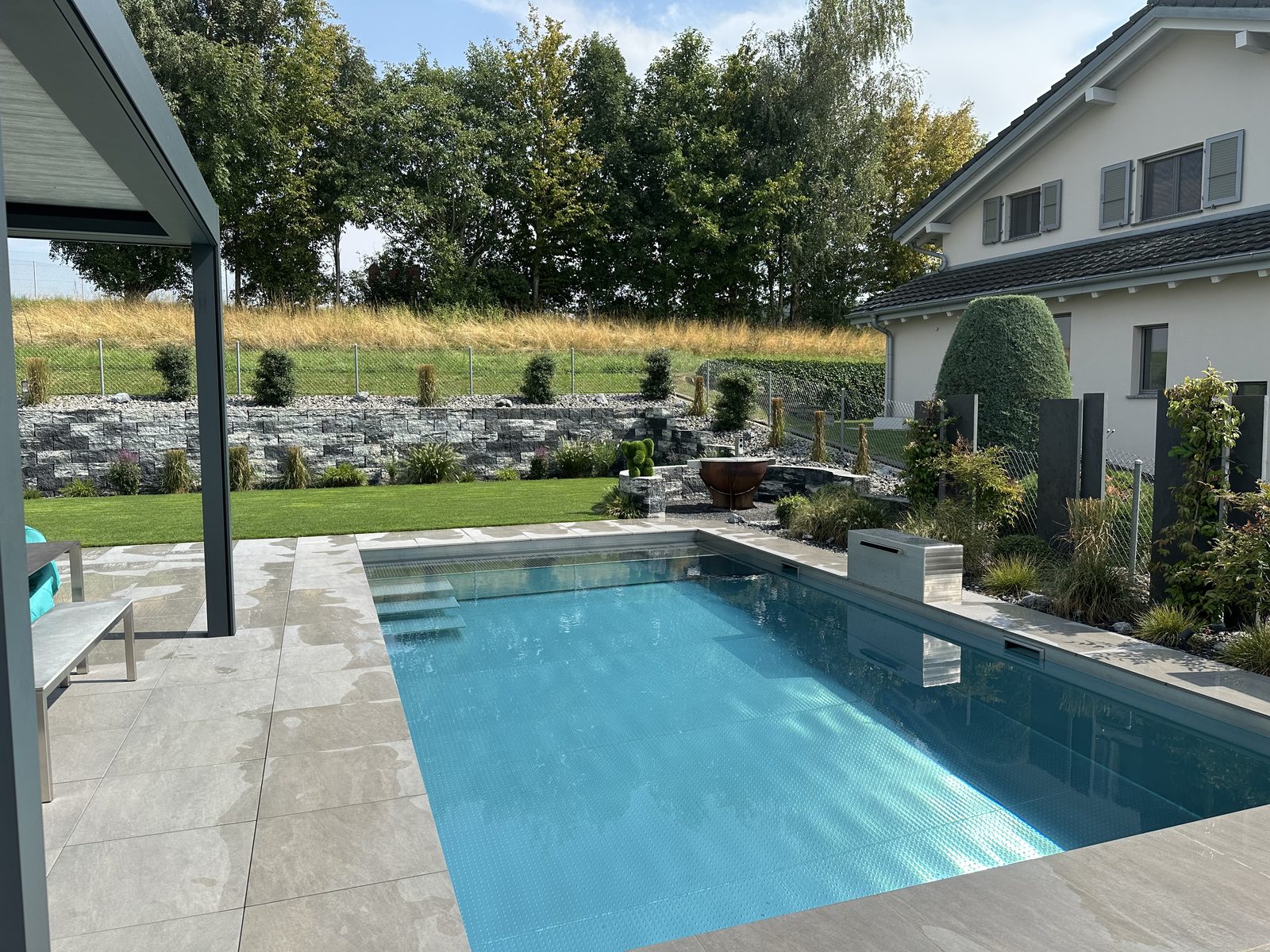 Stainless-steel pool with crystal-clear water, gabion wall and landscaped garden