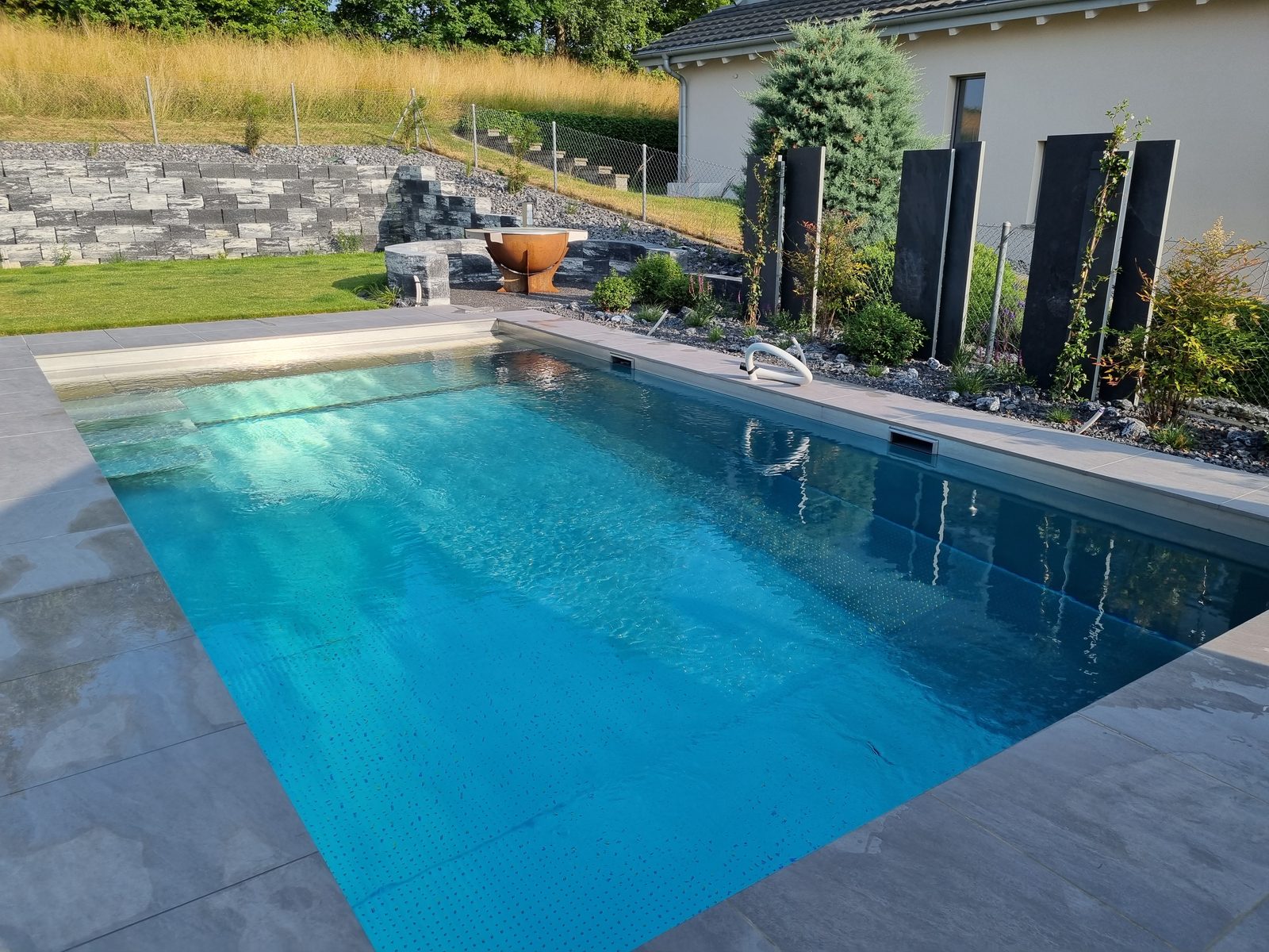 Turquoise water of the stainless-steel pool, corten fire pit and boulders
