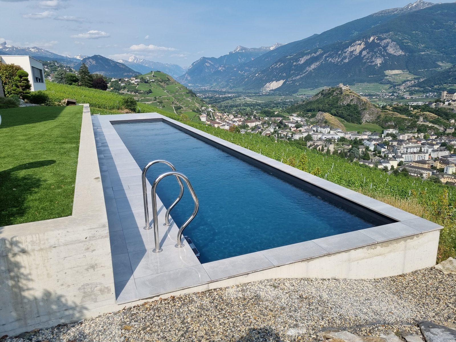 Couloir de nage rénové en PVC anthracite avec échelle inox, vue plongeante sur les vignes et les Alpes valaisannes