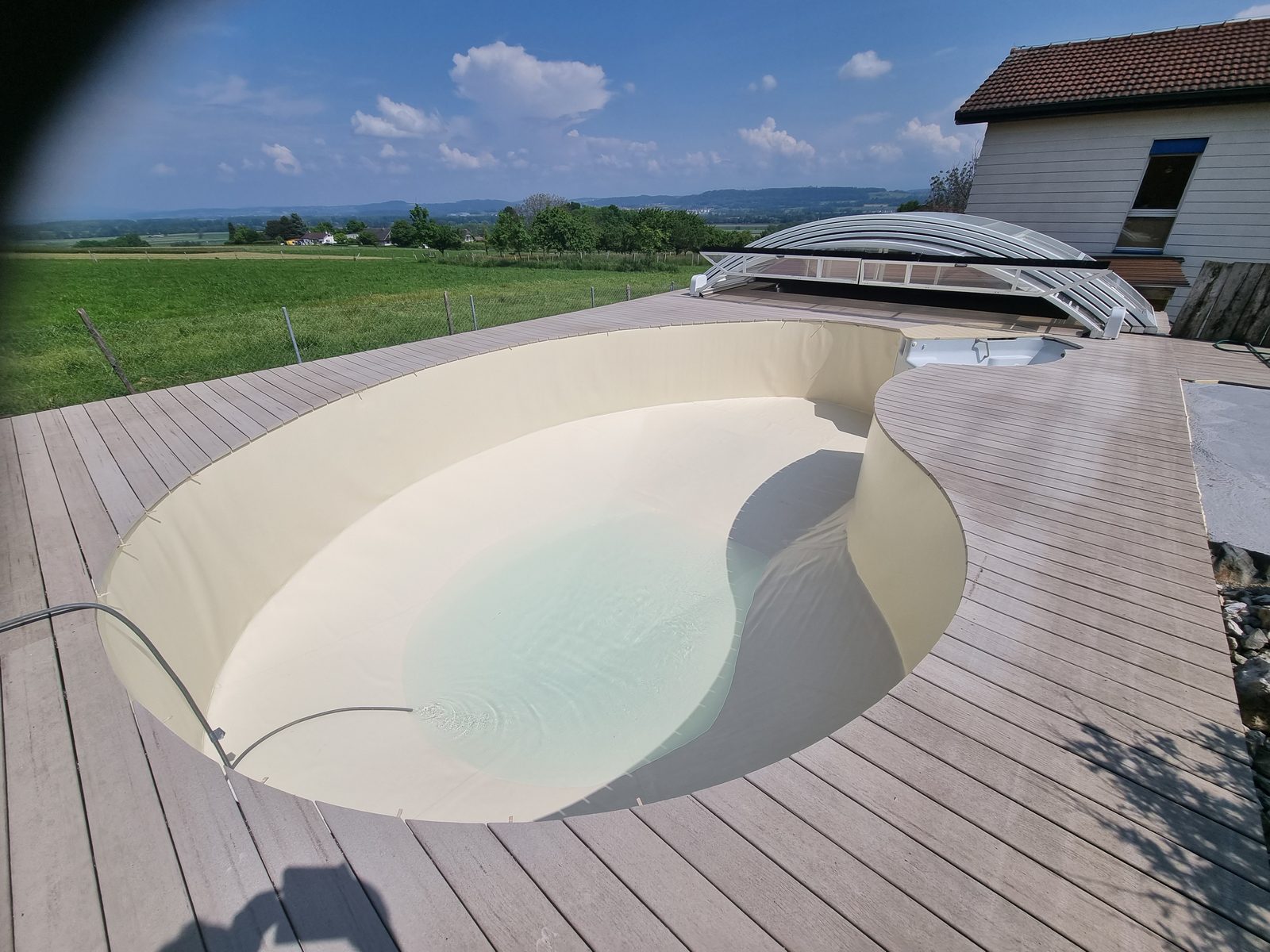 Piscine ronde rénovée en PVC armé beige sable sur terrasse composite, panorama campagne